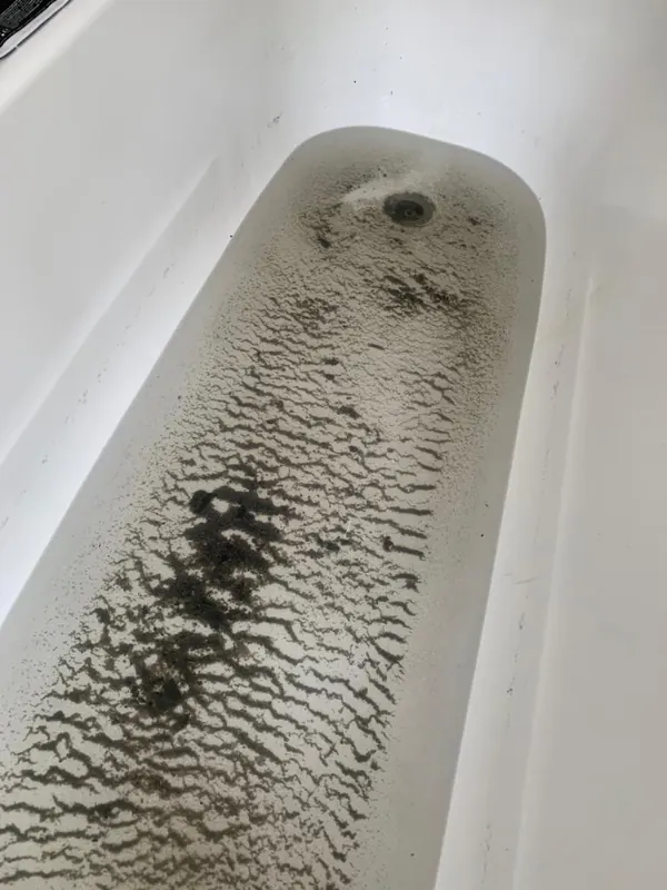 Baignoire avec des dépôts noirs refoulés par l'évacuation bouchée