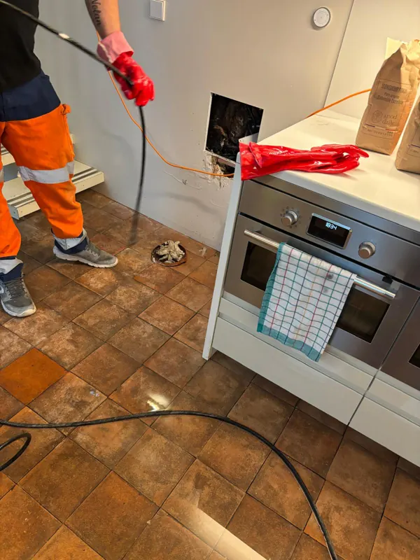 Technicien passant un flexible haute pression dans l'évacuation d'une cuisine