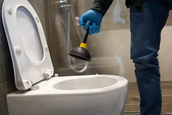 Plombier avec une ventouse devant un WC, prêt pour un débouchage en urgence