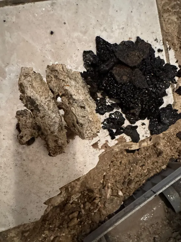 Blocs de calcaire et plaques de dépôts noirs sortis d'une canalisation après curage